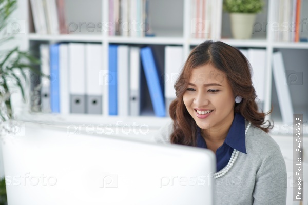 Pretty smiling Indonesian business woman looking at computer screen