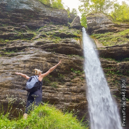Female hiker raising arms inhaling fresh air, feeling relaxed and free in beautiful natural environment under Pericnik waterfall in Vrata Valley in Triglav National Park in Julian Alps, Slovenia.