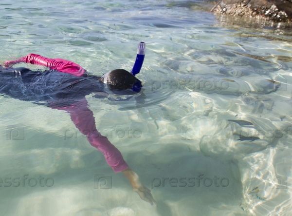 Asian girl reaches out for fish while snorkelling in clear sea water