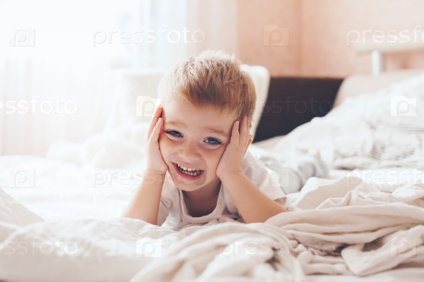 2 years old little boy dressed in pajamas are relaxing and playing in the parent\'s bed, warm and cozy scene. Pastel colors, selective focus.