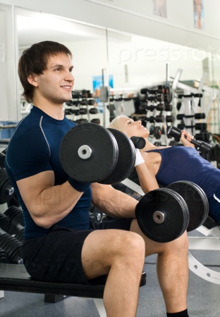 Happy cutie athletic girl and guy, exercise with dumbbells and smile, in sport-hall, stock photo