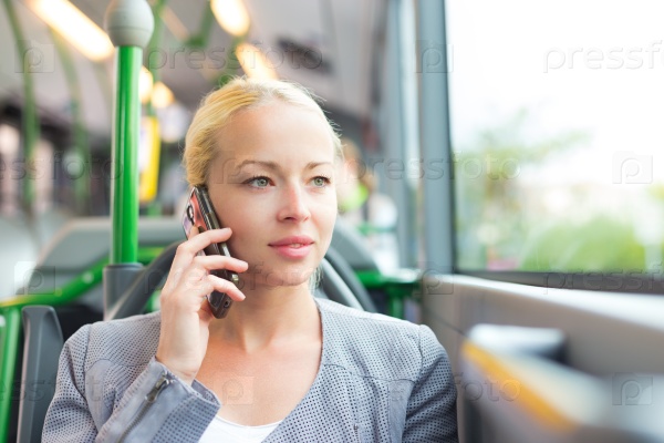 Blonde caucasian business woman talking on cell phone, traveling by bus. Public transport and commuting to work.