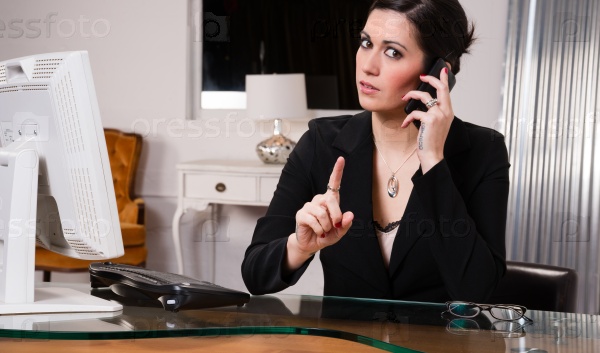 Woman at computer desks looks frustrated while talking on her cell phone