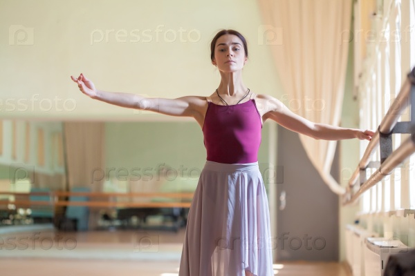 classic ballet dancer posing at barre on rehearsal room background
