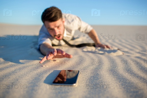 Poor signal. Frustrated young businessman searching for mobile phone signal while lying on sand in desert