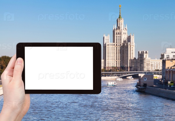Travel concept - hand holds tablet pc with cut out screen and Moscow vysotka - skyscraper on background, stock photo