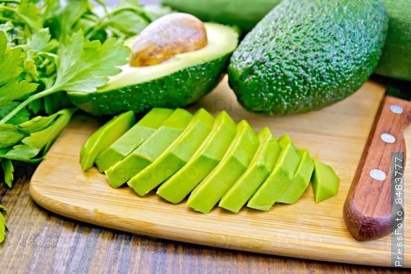 Whole and halved avocado, sliced avocado half, knife, parsley, napkin on a wooden boards background