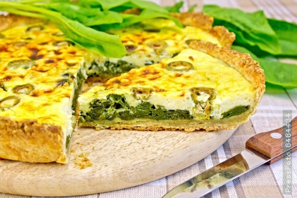 Pie with spinach, cheese and olives on a round board, spinach leaves, knife on background linen tablecloths, stock photo
