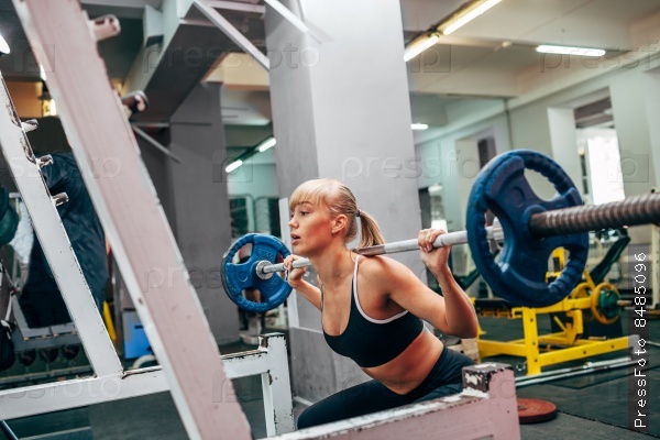 blonde strong fitness woman doing barbell squats in a gym