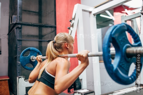 Blonde strong fitness woman doing barbell squats in a gym, stock photo
