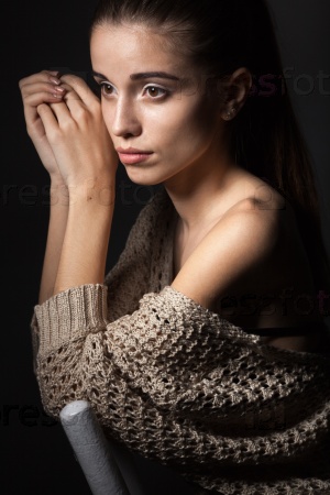 beautiful fashion model wearing hanging beige blouse sitting on chair over dark, looking faraway