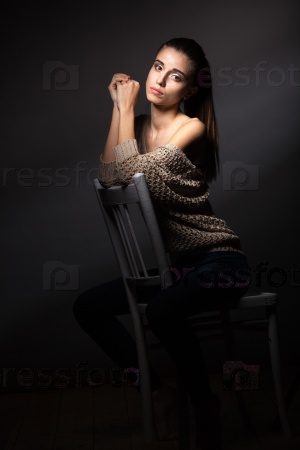 beautiful fashion model wearing hanging beige blouse sitting on chair over dark