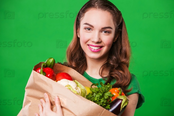 beautiful smiling woman holding a grocery bag full of fresh and healthy food. on green background