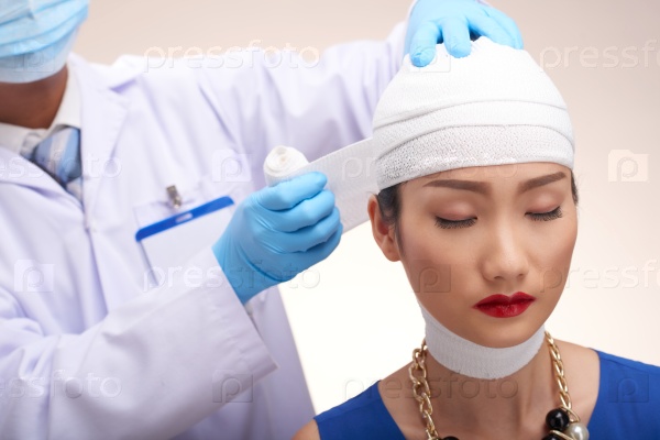 Plastic surgeon bandaging head of glamorous Chinese woman