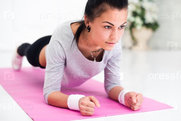 Pretty young woman doing plank abdominal exercise at home in white room.