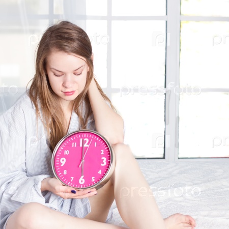 Young woman with alarm clock on the bed at morning