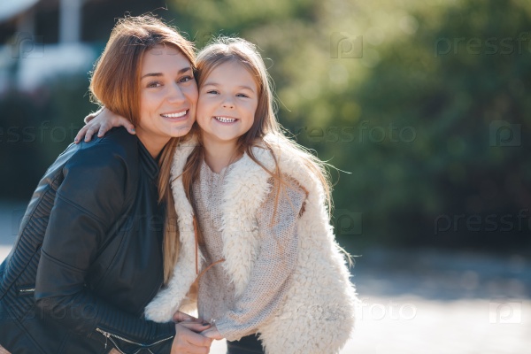 Fashion family concept - stylish mother and child wear. A portrait of a happy family: a young beautiful woman with her little cute daughter. Young daughter hugs mother in autumn city outdoor