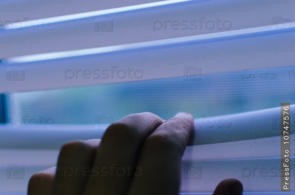 Hand separating slats of venetian blinds with a finger to see through