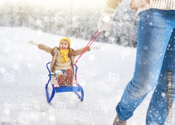 Child sledding. Parent rolls the child on a sled. Little girl enjoying a sleigh ride. Family plays outdoors in snow. Outdoor fun for family winter vacation, stock photo