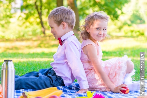 Boy and a girl of 6 years on a picnic sitting back to back, stock photo