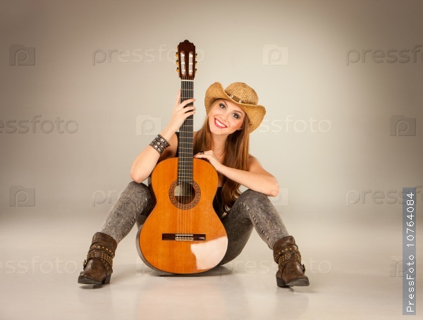 The beautiful girl in a cowboy\'s hat and acoustic guitar on a gray background, stock photo