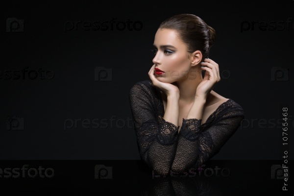 Beautiful young woman in lace top with red lips touching face. Over black background. Copy space.