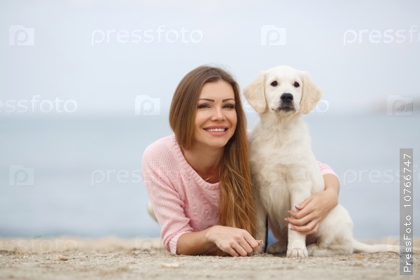 Portrait of beautiful young woman playing with dog on the sea shore. portrait of Young girl sitting on the ground with her dog retriever. woman with puppy. Girl with dog.
