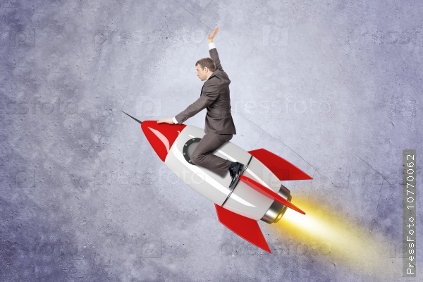 Businessman flying on red rocket on grey wall background, stock photo