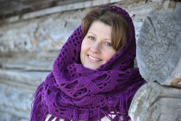 The Russian woman in a shawl warms hands near an izba, stock photo