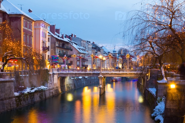 View of lively river Ljubljanica bank with Cobblers\' Bridge in old city center decorated with Christmas lights. Ljubljana, Slovenia, Europe. Shot at dusk.