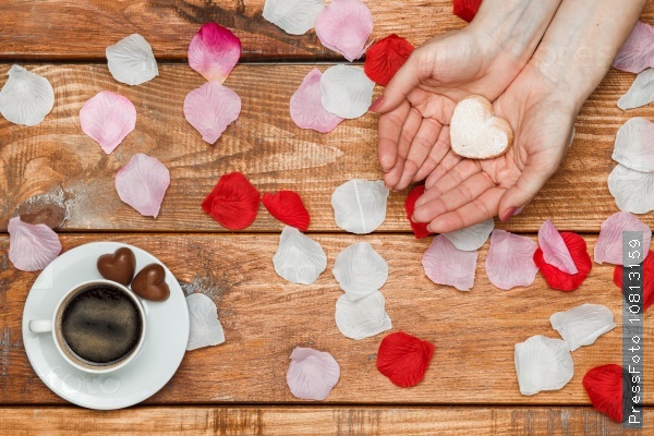 Valentines Day concept. Female hands with hearts on wooden background with flower petals and cup of coffee, stock photo