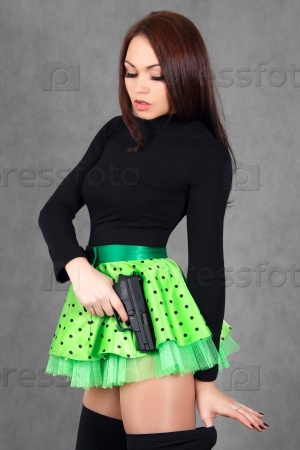 Portrait of a young attractive woman in a bright green skirt with a gun over grey background