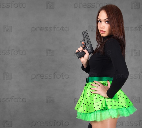 Portrait of a young attractive woman in a bright green skirt with a gun over grey background