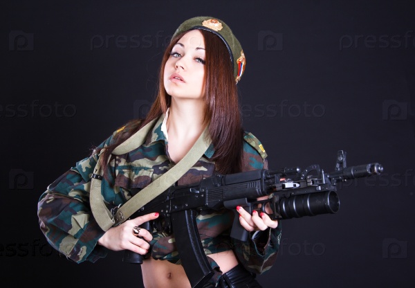 Young woman in the military uniform with the assault rifle over black background