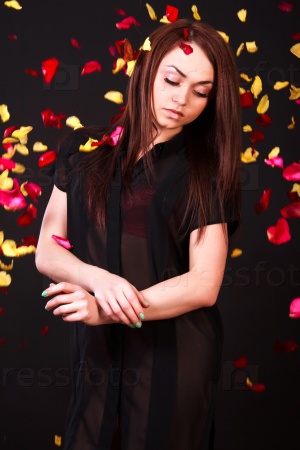 Beautiful young woman staying under the falling petals over black background
