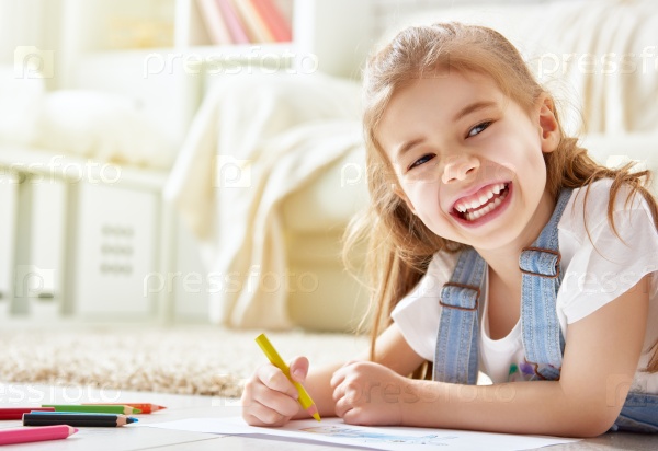 Happy child plays. Little child girl draws with colored pencils.