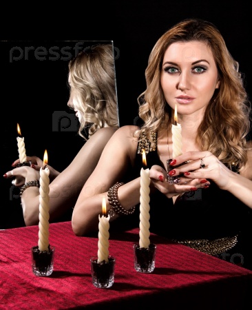 Beautiful young woman with candles near the mirror over black background