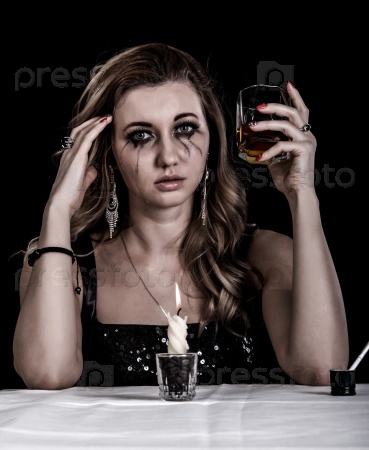 Depressed young woman with a glass of whiskey over black background