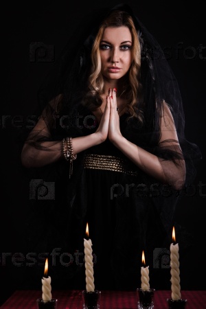 Praying young woman with candles in darkness