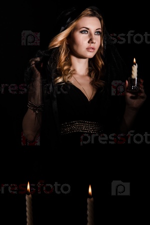 Mysterious young woman with a candle in darkness
