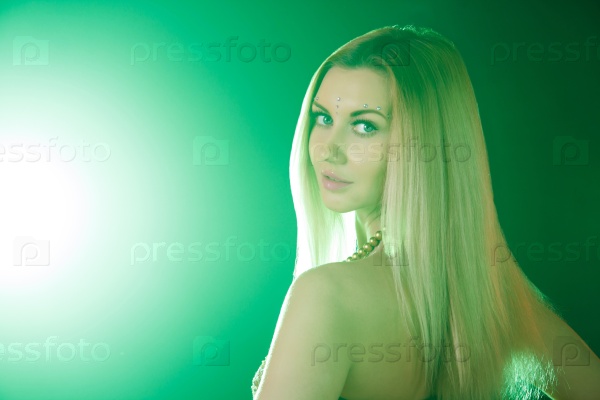 Beautiful young woman looks around at the backround of the bright green light