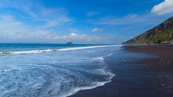 The beach with black volcanic sand on the island of Bali in Indonesia on a sunny summer day, stock photo