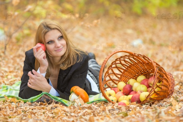 Young beautiful girl lies on the on the foliage in the autumn forest and dreaming holding an apple and looking to the right, stock photo