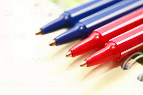 Closeup of four plastic pens on open spiral notebook, stock photo