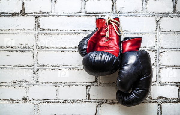 Pair of old red and black boxing gloves hanging on white brick wall.