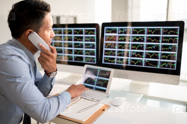 Stock market trader talking on telephone when looking at the monitor
