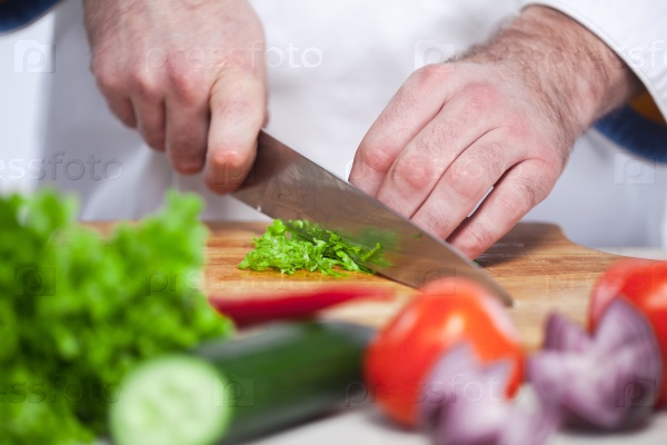 The hands of chef cutting a green lettuce in his kitchen on white background
