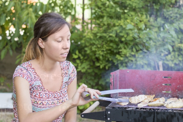 Handsome young woman preparing barbecue in the backyard