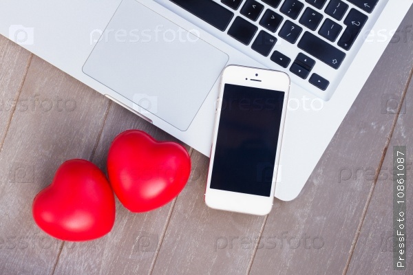 Styled desktop with modern phone, laptop and two red hearts, stock photo