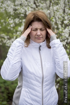 Adult woman with headache about bird cherry blossoms in spring
